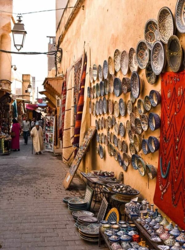 Traditional Moroccan medina street with local shops selling handmade ceramics, rugs, and crafts, showing daily life in Morocco’s old cities.