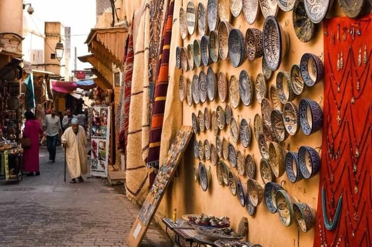 Traditional Moroccan medina street with local shops selling handmade ceramics, rugs, and crafts, showing daily life in Morocco’s old cities.