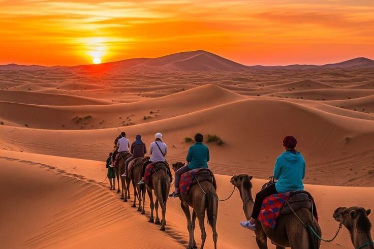 Travelers riding camels across Erg Chebbi dunes at sunset on a 9 day Morocco desert tour.