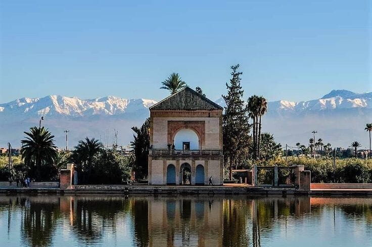Menara Gardens pavilion reflecting in water with Atlas Mountains in the background, a peaceful stop during a Marrakech cultural visit.
