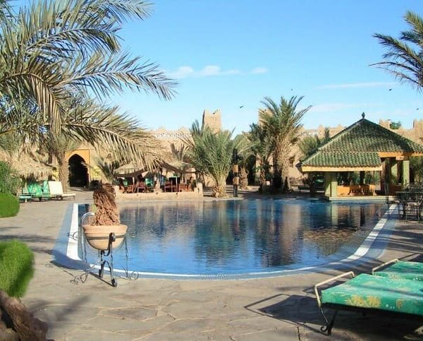 Desert hotel swimming pool surrounded by palm trees and traditional architecture in Merzouga Sahara Morocco