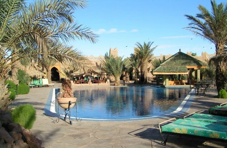 Desert hotel swimming pool surrounded by palm trees and traditional architecture in Merzouga Sahara Morocco