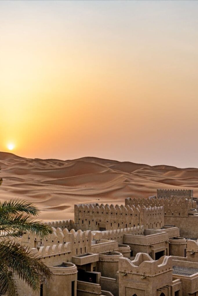 Sunset over golden sand dunes of Merzouga Sahara desert with traditional kasbah-style architecture in Morocco