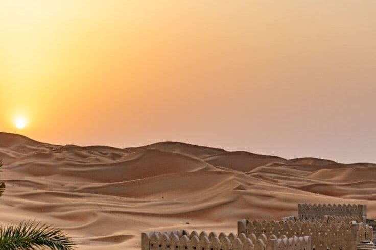 Sunset over golden sand dunes of Merzouga Sahara desert with traditional kasbah-style architecture in Morocco