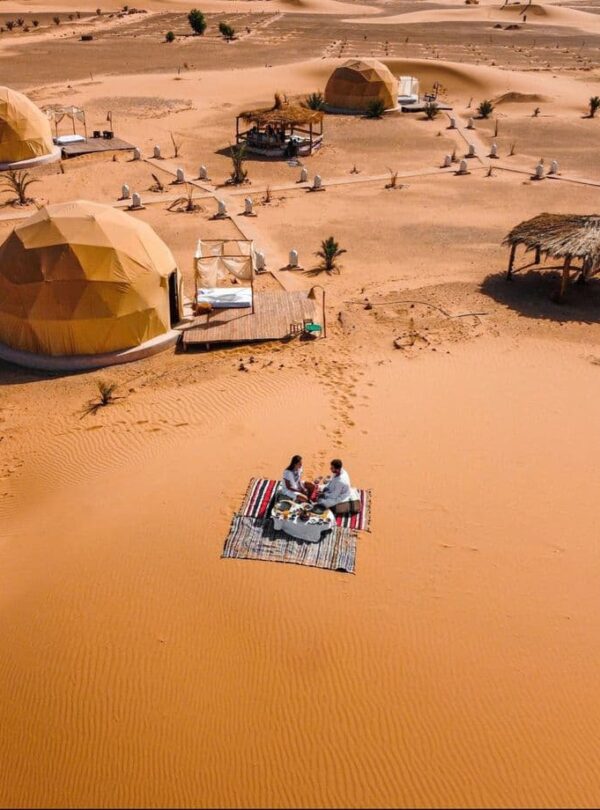 Couple enjoying private romantic dinner near luxury desert camp tents in Merzouga Sahara Morocco