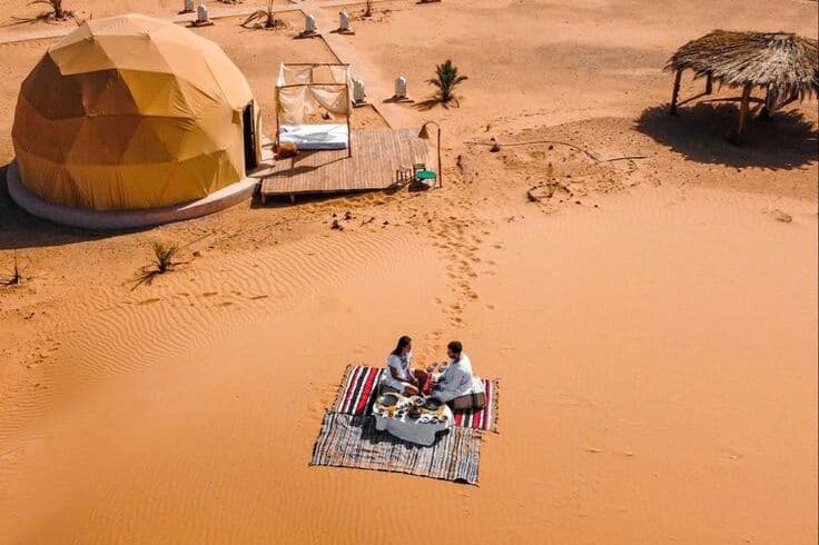 Couple enjoying private romantic dinner near luxury desert camp tents in Merzouga Sahara Morocco