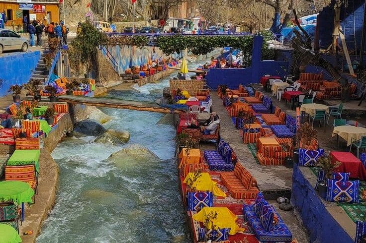 Colorful riverside cafés in Ourika Valley with snow-capped Atlas Mountains, popular day trip from Marrakech.