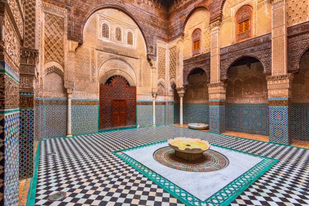 Historic madrasa courtyard with intricate Islamic tilework and carved arches in Fes Morocco