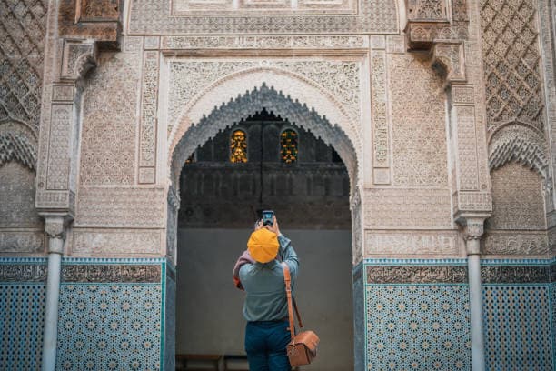 Traveler photographing ornate Islamic architecture inside historic madrasa in Fes Medina Morocco
